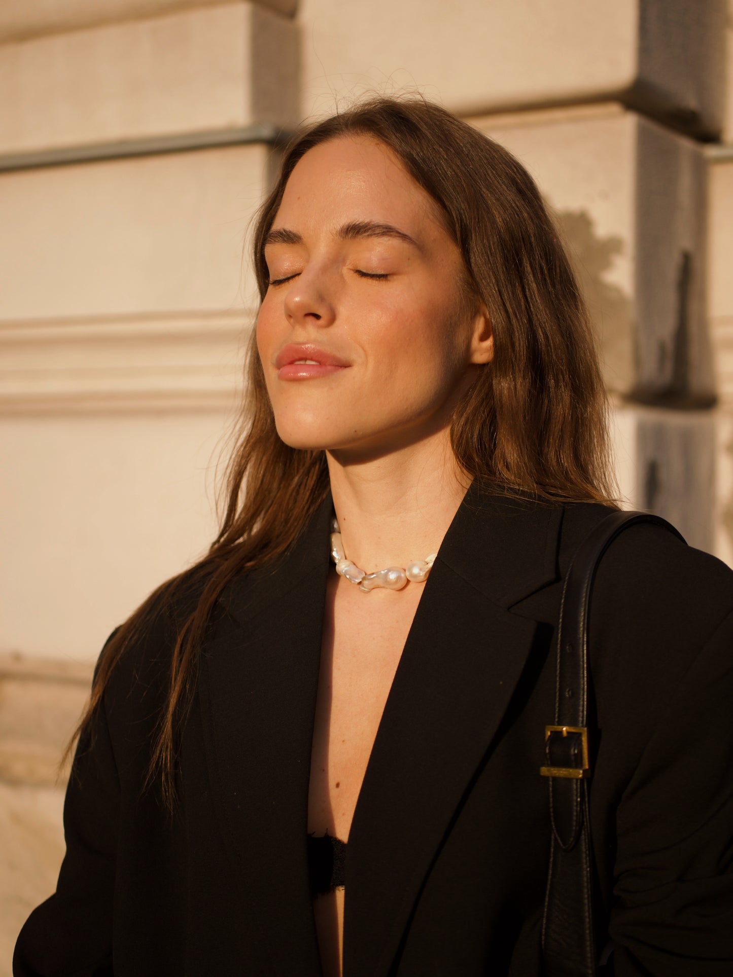 Woman wears bold Keshi pearl necklace and a black suit