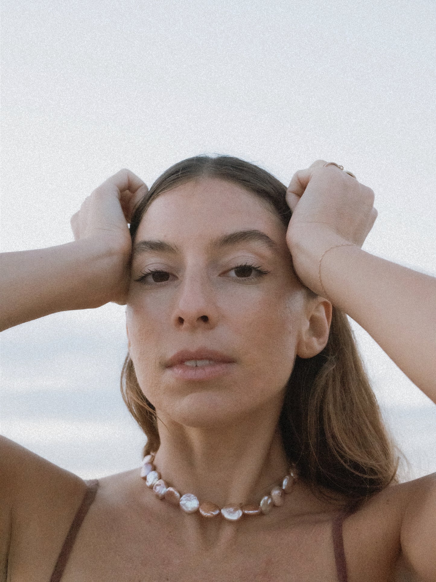 A person with a neutral facial expression, wearing a mauve-colored choker necklace with flat, rounded keshi pearls and 14k gold-filled components.