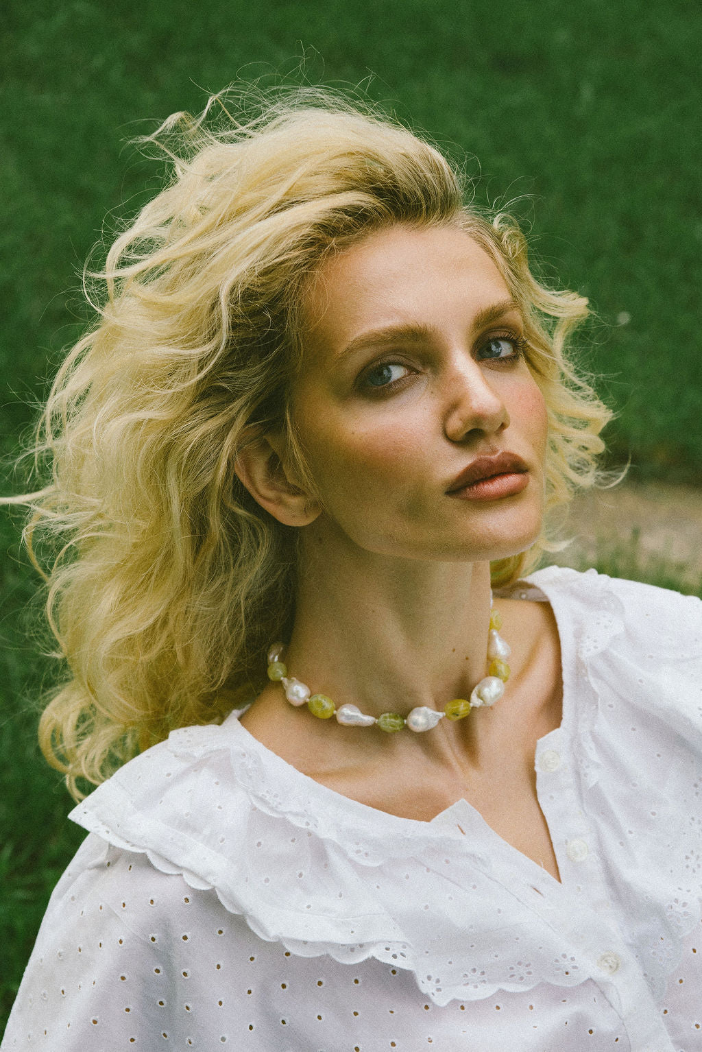 Woman with blonde hair wearing a white blouse and Keshi pearl necklace against a green background