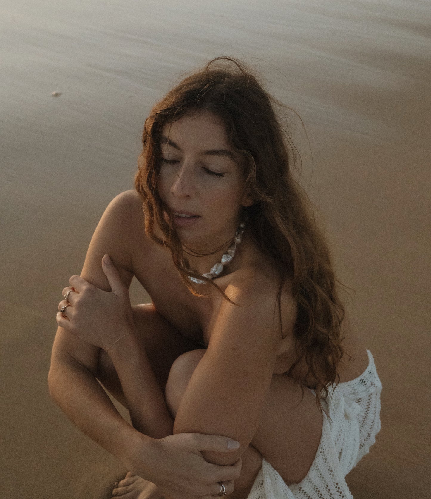 A person sitting on a sandy beach wearing a white top and a Keshi necklace with bold round beads.
