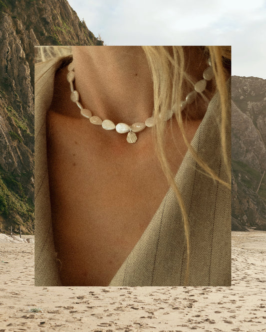 Keshi necklace made out of drop shaped pearls, worn by a blond girl with silver seashell pendant front of a mountain background. 