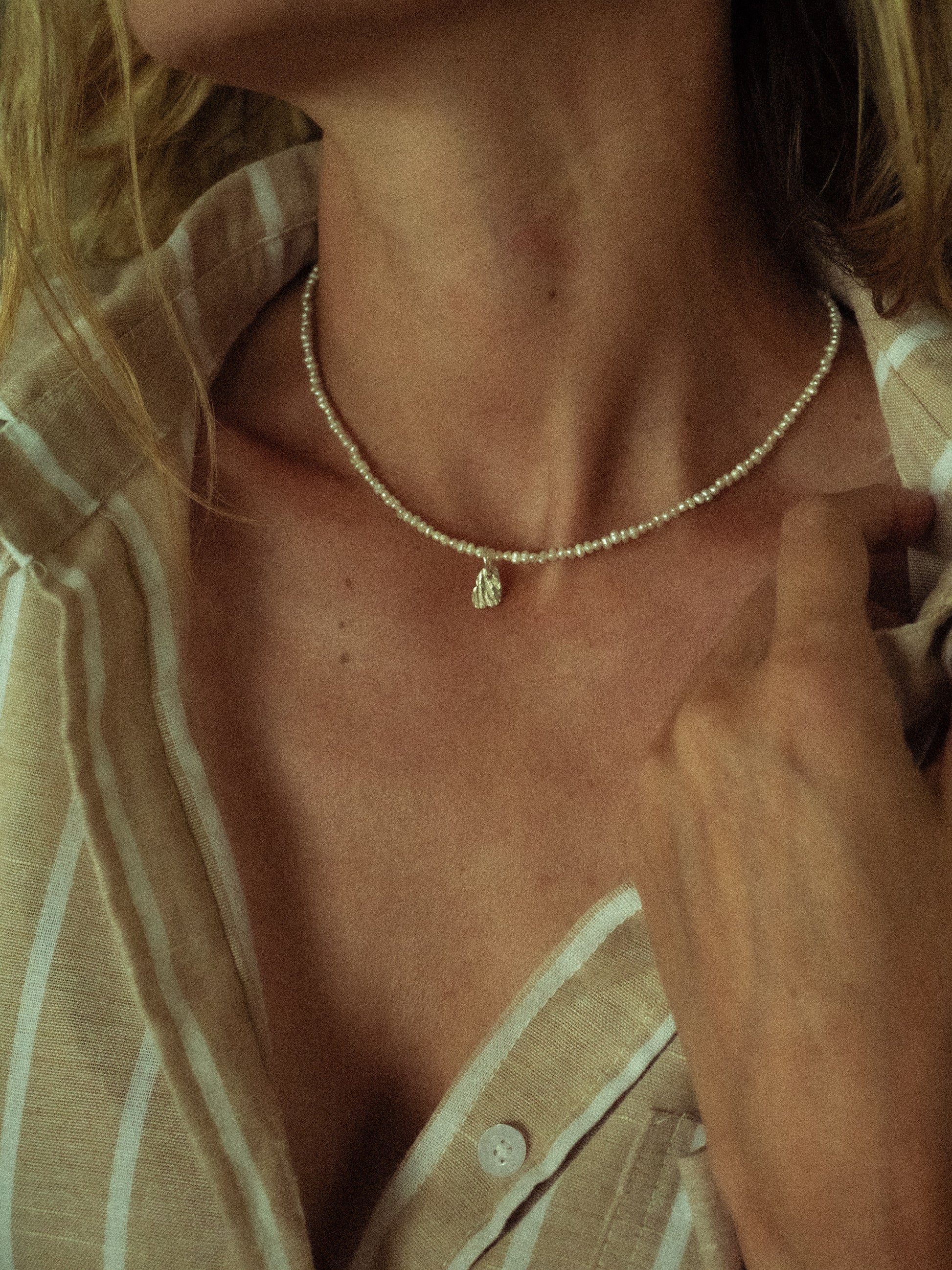 Person wearing a delicate seashell Keshi necklace with a small silver pendant, close-up shot.