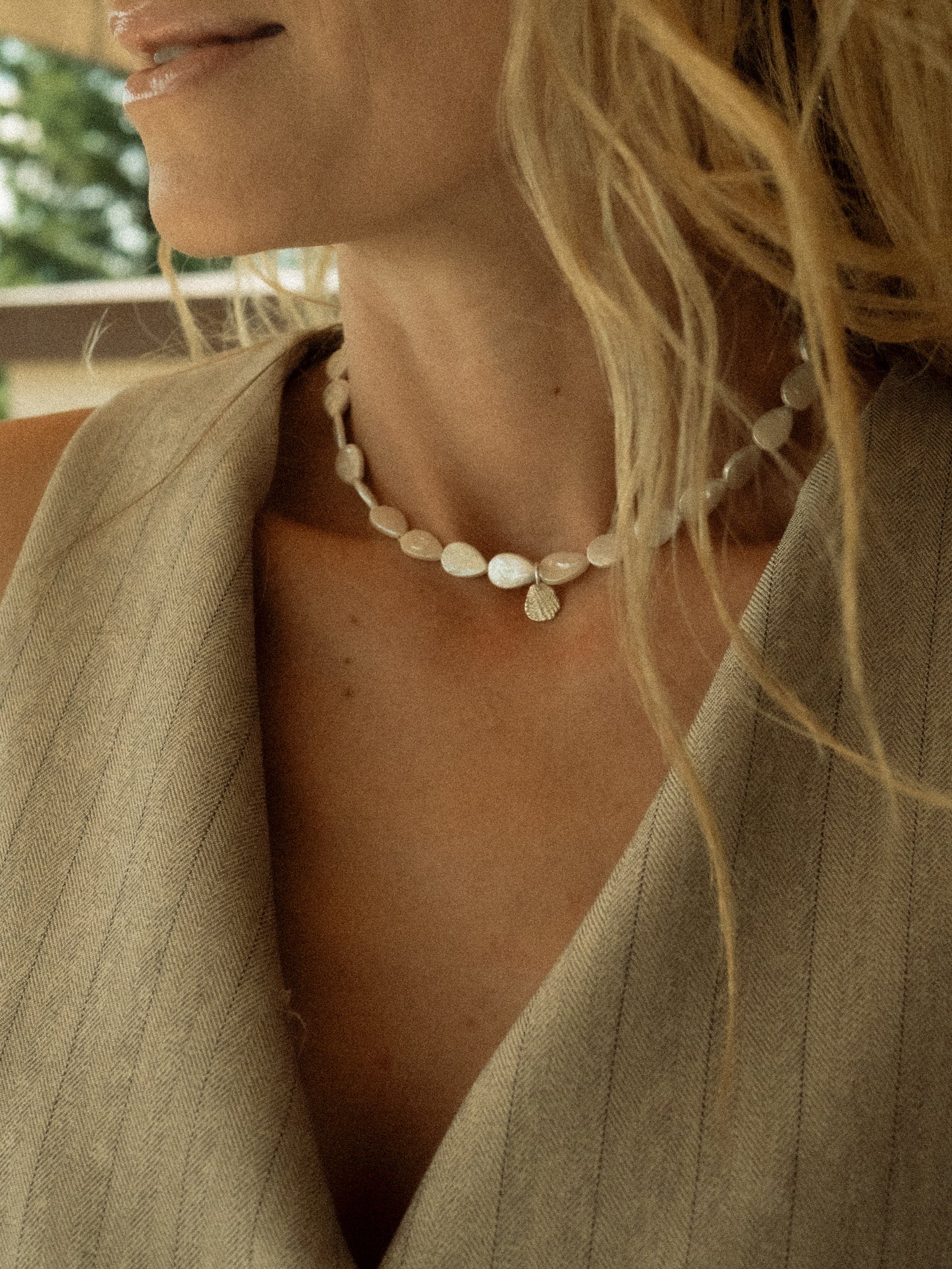 Keshi necklace made out of drop shaped pearls, worn by a blond girl with silver seashell pendant. 