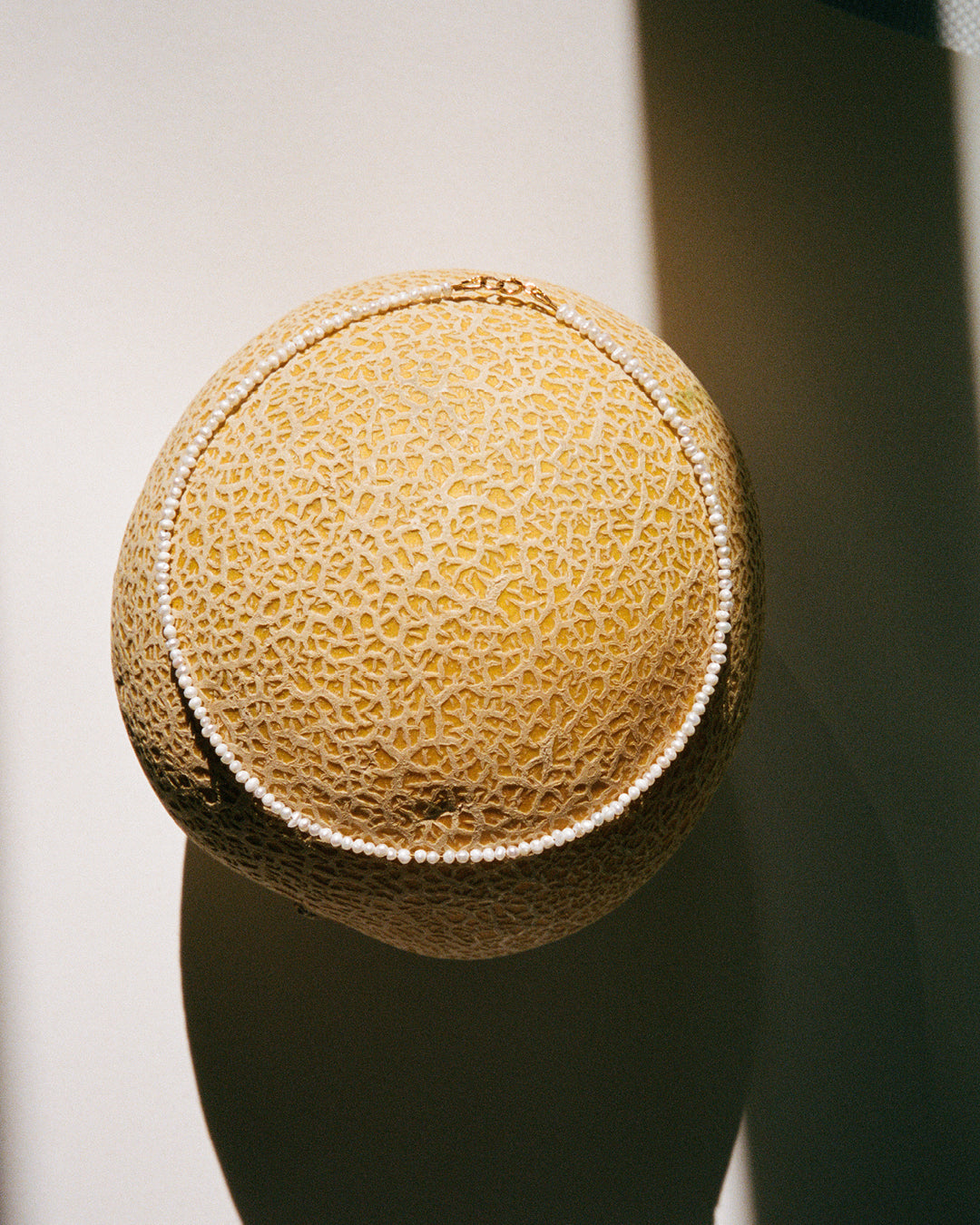 A close-up image of a delicate choker necklace with small Keshi beads and gold-filled components, displayed on a melon. 